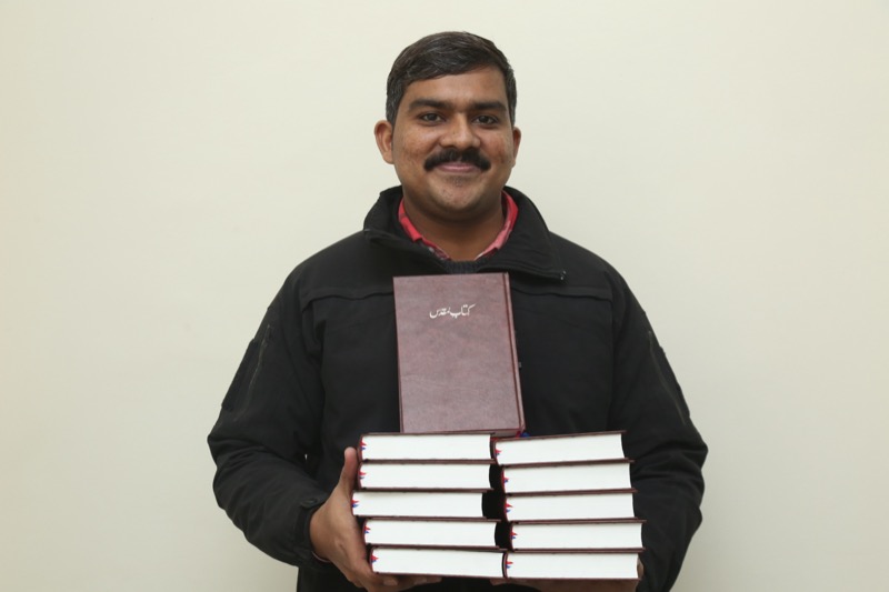 Pastor holding stack of free Urdu Bibles distributed by Good Samaritan Ministries Pakistan
